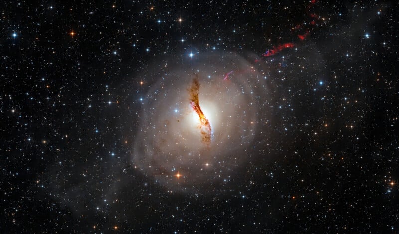 High-resolution image of a galaxy known as Centaurus A, with a bright core surrounded by a dark dust lane. Bright stars are scattered across the background and jets of red light emanate from the galaxy's center.